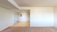 This single-story home offers a thoughtfully organized layout with four bedrooms, two bathrooms, a kitchen, a hallway, and a dedicated laundry room — all contained within an efficient and functional floor plan. The living area features warm neutral carpeting and white walls throughout, creating a clean, versatile canvas. A textured ceiling and an electrical panel are visible in the common area, which connects seamlessly to the rest of the home via a central hallway. The galley-style kitchen is equipped with light wood cabinetry, gray laminate countertops, tile flooring, and white appliances including a range and refrigerator, offering ample storage and prep space. Each of the four bedrooms is carpeted and features neutral walls, with several rooms benefiting from windows dressed with blinds that invite natural light and outdoor views. The primary bedroom provides a comfortable, well-proportioned space. The two bathrooms are functional and cleanly finished — one includes a standalone shower stall, while the other features a full tub-shower combination, both with wood-toned vanities and gray countertops. The dedicated laundry room includes utility hookups and built-in shelving overhead. Overall, the home presents a straightforward, no-frills design suited for practical, comfortable living.
