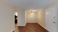 Located at 10612 Abercorn Extension in Savannah, Georgia, this single-floor property offers a clean, well-maintained living environment with a straightforward and functional layout. The main living area is highlighted by rich, warm hardwood-style flooring that extends throughout, creating a cohesive and inviting atmosphere. Neutral cream-toned walls provide a versatile backdrop suitable for a variety of interior styles. A ceiling fan with a light fixture is centrally positioned in the living space, offering both air circulation and ambient lighting. Clean white baseboards frame the room, adding a crisp contrast to the warm flooring below. The space flows openly into an adjacent area, visible through a connecting doorway, which appears to lead into a kitchen or dining space equipped with dark cabinetry and additional lighting. The overall design is practical and understated, emphasizing usability and comfort. The single-floor configuration makes the property highly accessible, with all living spaces conveniently located on one level. The property's location on Abercorn Extension places it within a well-connected corridor of Savannah, offering convenient access to local amenities, shopping, and services throughout the area.