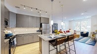 Located at 113 Ellington Blvd in Gaithersburg, MD, this modern one-bedroom, one-bathroom residence offers a thoughtfully designed layout across a single floor. The open-concept kitchen is a standout feature, showcasing sleek gray cabinetry, stainless steel appliances, subway tile backsplash, and a granite-topped island with pendant lighting and bar seating — ideal for both cooking and casual dining. Track lighting and warm hardwood flooring complete the kitchen's contemporary aesthetic.

The living room is bright and welcoming, with large windows that invite natural light and feature patterned accent wallpaper, adding a stylish touch to the space. The bedroom offers a comfortable retreat with plush carpeting, a dedicated window with outdoor views, and an accent wall with bold geometric wallpaper. A well-organized closet provides practical storage.

The bathroom is clean and modern, featuring a full tub and shower combination, a wide vanity with ample counter space, and tile flooring. Throughout the residence, the design balances contemporary finishes with warm, inviting details, creating a cohesive and comfortable living environment in the heart of Gaithersburg.
