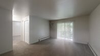 Located at 1844 Preston Ct NW in Walker, Michigan, this single-floor unit offers a practical and well-organized layout. The living room is a comfortable, open space finished with neutral-toned carpet and anchored by a large sliding glass door dressed with vertical blinds, allowing natural light to filter in while framing views of surrounding greenery. A wall-mounted air conditioning unit and baseboard heating provide year-round climate control. A tiled entryway leads into the living area, providing a clean transition from the front door into the carpeted main space.

The galley-style kitchen is efficiently designed with warm wood cabinetry lining both sides, offering generous storage above and below the counters. Gray laminate countertops, a double stainless steel sink, a white subway tile backsplash, and a stainless steel refrigerator complete the kitchen's functional setup. Tile flooring runs throughout this area for easy maintenance.

The bedroom is a well-proportioned, quiet room with carpeting, a window with blinds allowing natural light, and baseboard heating. The full bathroom features tile flooring, a wood-toned vanity with a light countertop, and a tiled shower-tub combination, offering a clean and functional design throughout.