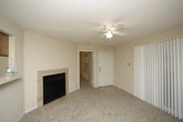 This single-story unit is designed with a functional, straightforward layout that connects living, dining, and sleeping areas cohesively. The living room serves as the central gathering space, highlighted by a tiled fireplace surround, a ceiling fan with integrated lighting, and textured ceilings throughout. Large vertical blinds cover a sliding door or wide window, allowing natural light to fill the room. The kitchen is arranged in a galley style, featuring white cabinetry with wood-trimmed accents, a double-basin sink, white appliances including a refrigerator and electric range, and stone-look tile flooring. A pass-through counter connects the kitchen to the living area, enhancing the open feel.

The bedrooms are carpeted and finished in neutral tones, each offering windows that bring in natural outdoor views. The primary bedroom includes a connected bathroom with a vanity, wood-front cabinetry, a mirror, and a tiled tub-shower combination. A second bathroom mirrors this layout, featuring a wide vanity countertop, above-toilet cabinetry, and a curtained shower. Consistent use of neutral carpet, textured ceilings, and white trim unifies the overall aesthetic throughout the space.