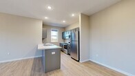 This contemporary two-story residence offers a clean, modern aesthetic throughout, with light-toned luxury vinyl plank flooring and neutral wall colors creating a bright, cohesive atmosphere across the main living areas. The open-concept kitchen is a standout feature, anchored by a peninsula with a white countertop and integrated sink, complemented by gray cabinetry and a full suite of stainless steel appliances including a refrigerator, electric range, microwave, and dishwasher. Recessed lighting illuminates the space efficiently, while a window above the sink brings in natural light. The kitchen flows seamlessly into a generous living area equipped with a ceiling fan and multiple windows that allow ample daylight and views of the surrounding neighborhood. The bedrooms are well-proportioned, with some featuring plush carpeting, ceiling fans, and large windows overlooking the exterior. One bedroom features hard surface flooring and a wall-mounted HVAC unit. The full bathroom includes a tub-shower combination, toilet, and a vanity with gray cabinetry and black hardware. The attached garage features a concrete floor, drywall-finished walls, an automatic garage door opener, and a window for natural light, offering practical utility and storage potential.