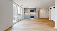 Located at 144 Roehampton Ave in Toronto's midtown neighbourhood, this modern studio unit offers a well-designed open-concept layout that maximizes every square foot. Light-toned hardwood flooring runs throughout, lending warmth and continuity to the space.

The living area is bright and airy, anchored by expansive floor-to-ceiling windows that frame sweeping views of the surrounding cityscape and flood the interior with natural light. Track lighting overhead adds functional illumination for evening use.

The kitchen is seamlessly integrated into the open living space and features sleek, flat-front cabinetry in a cool grey finish, stainless steel appliances including a range, built-in microwave, and refrigerator, complemented by a clean countertop and under-cabinet sink. The design is both contemporary and functional.

Sliding panel closets with high-gloss white doors provide generous built-in storage, maintaining the unit's clean, uncluttered aesthetic. The bathroom is a standout feature, finished with large-format marble-effect tiles covering the walls and floors, a deep soaking tub with chrome fixtures, and a toilet — all contributing to a spa-like atmosphere.

Overall, the unit presents a cohesive, minimalist design with high-quality finishes throughout, making it a refined and practical urban living space in the heart of Toronto.