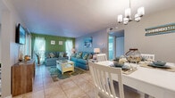 Located in Seminole, FL, this single-story, one-bedroom, one-bathroom home offers a cheerful coastal aesthetic carried consistently throughout every room. The open-concept living and dining area serves as the heart of the home, featuring light tile flooring, a bold green accent wall, and large windows that allow natural light to fill the space. A chandelier-lit dining nook provides an intimate setting for meals, positioned just steps from the kitchen. The kitchen is equipped with white cabinetry, granite-style countertops, and stainless steel appliances, offering a clean and functional layout with direct sight lines into the dining area. The bedroom is a comfortable retreat with plush carpeting, multiple windows dressed in sheer white curtains, and a soothing aqua accent wall that reinforces the beach-inspired theme. The full bathroom includes a tub-shower combination, white vanity cabinetry, and tile flooring. A dedicated laundry area houses a stacked washer and dryer unit for added convenience. The screened patio extends the living space outdoors, offering views of mature trees and tropical landscaping — a peaceful spot to relax and enjoy the Florida surroundings.