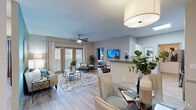 This single-floor residence offers a thoughtfully designed open-concept layout where the living, dining, and kitchen areas flow seamlessly together. The living room is anchored by a ceiling fan, wood-look flooring, and a set of French doors that invite natural light and provide outdoor access. A teal accent wall adds a bold design element, complementing the neutral palette used throughout the space. The dining area features a round glass-top table beneath a large drum pendant light, with a framed mirror and wall art enhancing the room's character.

The galley-style kitchen is well-equipped with stainless steel appliances, including a refrigerator, dishwasher, microwave, and range. White upper cabinetry contrasts with gray lower cabinets, and granite-style countertops run along both sides. A pass-through to the laundry area adds functional convenience.

The two bedrooms are each distinct in style. One features soft gray tones with large windows offering natural views, while the second showcases a vibrant teal accent wall with warm wood furnishings. Both bathrooms include granite vanities, wood-look tile flooring, and a tub-shower combination, offering a clean and cohesive aesthetic throughout.