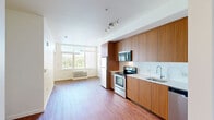 Located at 3750 South River Parkway in Portland, Oregon, this one-bedroom, one-bathroom unit offers a well-designed, efficiently laid-out living space with modern finishes throughout. The open-concept kitchen and living area forms the heart of the unit, featuring warm wood-grain flat-front cabinetry extending floor to ceiling, stainless steel appliances including an electric range, over-the-range microwave, refrigerator, and dishwasher, complemented by clean white countertops and a white tile backsplash. Rich hardwood-style flooring runs continuously throughout the space, adding warmth and visual cohesion. A large window at the end of the living area fills the room with natural light and provides a view of surrounding greenery. The bedroom is a comfortable, well-proportioned space with its own window framing a scenic view of the river and lush tree line — a standout feature of the unit. Two closets provide practical storage solutions. The bathroom continues the cohesive design aesthetic with matching wood-grain cabinetry, a large vanity mirror, white countertop with an undermount sink, and a clean, functional layout. The unit's consistent use of warm tones and modern finishes creates a bright, contemporary living environment.