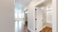 This thoughtfully designed one-bedroom, one-bathroom unit offers a cohesive and modern aesthetic across its single floor. Warm hardwood-style flooring flows continuously throughout, creating a unified and inviting atmosphere from room to room. A sleek hallway with sliding barn doors accented by matte black hardware provides a stylish entry point into the living areas.

The open kitchen and living area is a standout feature, showcasing two-tone cabinetry with soft teal lower cabinets and crisp white uppers, complemented by gold hardware and a white hexagonal tile backsplash. Light quartz countertops, a deep single-basin sink with a gold faucet, and a full suite of stainless steel appliances round out this well-appointed kitchen. Natural light pours in through large windows fitted with blinds, brightening the combined living space.

The bedroom is a calm, neutral retreat with warm beige walls, a ceiling fan, a double-door closet, and a window that brings in natural light. The bathroom continues the unit's refined design language, featuring a teal vanity with gold fixtures, white subway tile surrounding the soaking tub and shower, a large mirror, and coordinating black and gold hardware accents. Clean lines and consistent finishes make this a highly functional and visually cohesive living space.