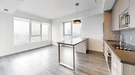 This thoughtfully designed 2-bedroom, 4-bathroom unit offers a clean, contemporary aesthetic across a single floor. The open-concept living and dining area is anchored by large floor-to-ceiling windows that frame sweeping city skyline views, flooding the space with natural light. Grey wood-look flooring runs consistently throughout, complementing the bright white walls for a cohesive modern look.

The kitchen is well-appointed with two-toned cabinetry in grey and wood finishes, dark quartz countertops, stainless steel built-in appliances including a wall oven and microwave, a glass tile backsplash, and a wine fridge. A peninsula with matching countertop doubles as a dining surface beneath a stylish gold-accented pendant light.

The bedrooms are bright and serene, with the primary bedroom featuring a large window overlooking the city. Two hallways connect the rooms efficiently. The four bathrooms are finished with large-format grey tiles; some feature a glass-enclosed walk-in shower, while others include a soaking tub with overhead shower. Vanities throughout feature wood-grain cabinetry with integrated white sinks.

A private balcony with glass railings and brick accent walls offers additional outdoor space with panoramic urban views, completing this modern high-rise unit.