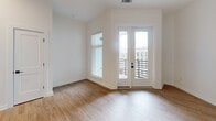 Located at 1711 Commonwealth Ave in Charlotte's vibrant Plaza Midwood neighborhood, this thoughtfully designed one-bedroom, one-bathroom residence offers a clean, modern aesthetic throughout. Light wood-look flooring flows continuously through the space, complementing the crisp white walls and black accent hardware found in every room.

The open-concept kitchen and dining area serves as the heart of the home, showcasing a striking two-tone cabinet design with white upper cabinetry and warm wood-toned lower cabinets, a herringbone tile backsplash, and a large central island topped with elegant white marble-veined quartz. Stainless steel appliances and a matte black faucet complete the chef-ready setup. Dramatic pendant lights hang above the island, adding a bold design statement. French doors open from the living area to a private patio with a modern slatted railing, offering open views of the surrounding Charlotte skyline.

The bedroom features high ceilings, a ceiling fan, and a horizontal band of black-framed windows that bring in natural light while maintaining privacy. Three closets, including a walk-in with wire shelving, provide generous storage. The bathroom includes a tub-shower combination with white tile surround and matte black fixtures. Recessed lighting and thoughtful finishes make this a polished, move-in-ready residence.