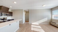This single-floor unit offers a clean, contemporary design characterized by neutral warm-greige walls, light wood-look plank flooring, and white trim that flows consistently throughout the space. The open living area is generously proportioned, bathed in natural light through multiple windows with horizontal blinds, and features recessed and flush-mount ceiling lighting. A private exterior door in the living area provides convenient direct access to the outdoors.

The kitchen is thoughtfully designed with rich dark-brown shaker-style cabinetry, brushed nickel hardware, and crisp white countertops. Stainless steel appliances — including a refrigerator, range, and built-in microwave — lend a modern, functional aesthetic. The layout offers ample counter space and cabinetry for storage.

The bedroom is well-lit by multiple windows that invite natural light, continuing the same cohesive flooring and neutral palette seen throughout the unit. The bathroom includes a dark-cabinet vanity with a white countertop and undermount sink, a large mirror, and a shower-tub combination. A dedicated laundry closet houses a full-size top-load washer and dryer alongside the water heater, adding practical convenience to this well-designed space.