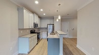 The Spring floor plan is a well-appointed 2-bedroom, 2-bathroom residence spread across a single level, designed with a modern aesthetic and functional layout. The open-concept kitchen serves as a central hub, featuring crisp white shaker cabinetry, granite countertops, a tile backsplash, and a full suite of stainless steel appliances. A large kitchen island with an integrated sink and pendant lighting above provides additional workspace and a natural gathering point that flows seamlessly into the living area. The living space is bright and open, with light hardwood-style flooring and French doors that invite natural light and offer outdoor access. Both bedrooms are generously sized, carpeted for comfort, and equipped with ceiling fans and windows that provide pleasant exterior views. Each bathroom is finished with granite-topped vanities featuring sage-toned cabinetry and tile flooring. The primary bathroom includes a walk-in closet with built-in shelving. The second bathroom features a tub-shower combination. Neutral wall tones and clean white trim throughout lend the residence a cohesive, move-in-ready feel that is both modern and welcoming.