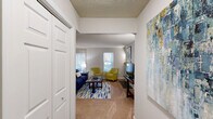 This well-appointed one-bedroom, one-bathroom residence in Greensboro, NC offers a thoughtfully designed single-floor layout with a comfortable, functional flow throughout. The living room serves as a welcoming centerpiece, highlighted by a striking stacked-stone fireplace with a wood mantel and multiple windows that fill the space with natural light. Adjacent to the living area, the dining space features hardwood-style flooring, a pendant light fixture, and a sliding glass door that opens to an outdoor patio. The kitchen is open and practical, featuring warm wood cabinetry, a mosaic tile backsplash, a breakfast bar peninsula, and black appliances including a range and refrigerator. The bedroom is carpeted and generously proportioned, offering natural light through large windows and direct access to a dedicated walk-in closet. The bathroom includes a warm wood vanity with ample countertop space, a wide mirror, a multi-bulb vanity light fixture, and hardwood-style flooring. Additional functional spaces include an entrance, hallway, and in-unit laundry, contributing to the overall convenience of the layout. Neutral tones and consistent finishes throughout create a cohesive and inviting ambiance.