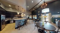 Located at 7938 City Base Landing in San Antonio, TX, this single-floor community clubhouse is designed with a bold, contemporary aesthetic that balances sophistication and functionality. The centerpiece of the space is an expansive open-plan lounge area crowned by dramatic vaulted ceilings with exposed dark beam accents and striking sputnik-style chandeliers that add a mid-century modern flair. Deep navy accent walls contrast beautifully with light-toned parquet-style flooring, creating a visually dynamic environment throughout.

The fully equipped kitchen features dark espresso cabinetry, a mosaic tile backsplash, granite countertops, stainless steel appliances, and a large peninsula bar with seating — ideal for social gatherings. Globe pendant lights overhead add a warm, inviting glow to the kitchen area. The main lounge is furnished with multiple seating arrangements, including leather accent chairs, round dining tables, and a cozy lounge vignette near the entrance, which benefits from abundant natural light through large windows and glass double doors.

A dedicated business center, accessible through framed glass doors, provides a quiet workspace. An adjacent private conference room offers a refined setting with a substantial wood-topped table, leather seating, and an orbital chandelier. Together, these spaces deliver a well-rounded, amenity-rich environment suited for both productivity and relaxation.