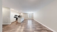 This efficiently laid-out 2-bedroom, 1-bathroom single-story unit offers a clean, modern aesthetic with a cohesive design throughout. The open-concept living and kitchen area serves as the heart of the home, anchored by a striking white kitchen island with a marble-look countertop and an integrated sink. White shaker-style cabinetry lines the kitchen walls, complemented by a full suite of stainless steel appliances, including a refrigerator with ice maker, electric range, and over-the-range microwave. Recessed lighting illuminates the space, while wood-look plank flooring extends seamlessly through every room, adding warmth and continuity. The living area is bright and open, with neutral warm-gray walls and a window that allows natural light to filter in. Both bedrooms are comfortably sized, each featuring natural light from windows with blinds and the same consistent flooring and neutral palette. The full bathroom is clean and functional, equipped with a tub-shower combination. A utility room provides additional convenience, housing the water heater and utility connections. The layout is completed by a connecting hallway that ties all rooms together in a practical, efficient flow.