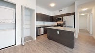 This single-floor unit showcases a contemporary design with a cohesive aesthetic throughout. The open-concept kitchen serves as a central highlight, featuring dark espresso-toned cabinetry paired with speckled granite countertops that extend across a spacious island, ideal for additional prep space or casual dining. Stainless steel appliances, including a refrigerator, range, microwave, and dishwasher, complete the kitchen's modern appeal. Light wood-tone luxury vinyl flooring flows seamlessly through the kitchen and into the open living area, which benefits from a large sliding glass door fitted with vertical blinds, allowing generous natural light to fill the space.

Adjacent to the kitchen, a dedicated storage closet with built-in shelving provides added organizational functionality, while a stacked in-unit washer and dryer offers added convenience. The bedrooms are bright and neutral, with windows fitted with horizontal blinds. The bathrooms mirror the kitchen's design language, featuring dark wood vanities, granite countertops, large-format tile flooring, and full-size soaking tubs with tiled surrounds. A second bathroom includes a frameless glass door entry and a well-lit vanity mirror, reinforcing the unit's clean, modern character throughout.