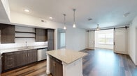 Located at 1601 Scottsdale Ln in Austin, TX, this well-appointed 2-bedroom, 2-bathroom single-story home offers a thoughtfully designed open-concept layout. The kitchen serves as the heart of the home, showcasing a granite-topped center island with pendant lighting overhead, dark espresso cabinetry, stainless steel appliances including a refrigerator, range, microwave, and dishwasher, all set atop durable hardwood-style flooring. The kitchen flows seamlessly into the living room, which features a ceiling fan, natural light from a large window, and a striking sliding barn door that adds a modern farmhouse touch. Both bedrooms are comfortably carpeted and receive natural light through well-sized windows, with the primary bedroom offering a dedicated closet. The primary bathroom includes a walk-in glass shower, granite vanity with dark cabinetry, and hardwood-style flooring, while the second bathroom mirrors the same quality finishes with a single vanity and a full bath. A dedicated laundry room houses a full-size washer and dryer with overhead shelving for added storage. Two closets and a hallway complete the practical layout of this clean, modern Austin home.