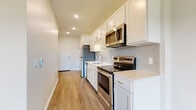 This single-floor residence offers a clean, contemporary design with consistent wood-look flooring throughout, neutral wall tones, and recessed lighting that create a bright and welcoming atmosphere. The galley-style kitchen is thoughtfully appointed with crisp white shaker cabinetry, light stone countertops, a subway tile backsplash in a soft gray-blue hue, and a full suite of stainless steel appliances including an electric range, built-in microwave, and refrigerator. A stainless steel undermount sink with a modern faucet completes the functional layout, while recessed lighting ensures the space is well-lit from end to end. Adjacent to the kitchen, the open living and dining area benefits from a large window that brings in generous natural light, lending the space an airy, comfortable feel. The bedroom continues the cohesive design with a bold blue accent wall, a large window with outdoor views of greenery, and the same wood-look flooring. The bathroom is finished with wood-toned cabinetry, a marble-look countertop, a large rectangular mirror, and tile flooring, offering a serene and polished retreat. Throughout the unit, clean lines and modern finishes create a cohesive and move-in-ready living environment.