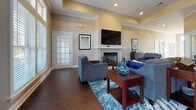 Located on Ravensclaw Lane in Fredericksburg, Virginia, this single-floor community space is thoughtfully designed to offer a range of functional areas within a cohesive, welcoming environment. Warm neutral tones, crown molding, and recessed lighting carry throughout, creating a consistent and polished aesthetic.

The expansive lounge area serves as the heart of the space, featuring rich hardwood flooring, a fireplace with a clean white surround, tray ceilings, and a wall-mounted television. Large windows along one wall flood the room with natural light, while a ceiling fan adds to the comfortable atmosphere. An adjacent dining area accommodates a full-sized table and flows seamlessly toward a pass-through kitchen outfitted with dark cabinetry, black granite countertops, warm hardwood flooring, and stainless steel appliances.

The fitness center is notably well-equipped, spanning multiple connected areas. One section houses cardio machines—including treadmills, ellipticals, and a stationary bike—alongside wall-mounted televisions and mirrors. A second area provides strength-training equipment, stability balls, and rubber flooring, with ample natural light from multiple windows.

A dedicated office and library space rounds out the facility, offering built-in shelving, patterned carpet, plantation shutters, and a workstation setup, making it ideal for productive use.