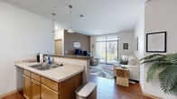 Located at 18-26 S Bedford St in the heart of Madison, WI, this efficiently designed single-floor unit combines a kitchen and living area into one cohesive, open-plan space. The kitchen is well-appointed with warm maple cabinetry, a double-basin sink, a full suite of black appliances including a refrigerator and range, a stainless steel microwave, and a breakfast bar with a granite-style countertop that seats two — ideal for casual dining or working from home. Pendant lighting above the bar adds a welcoming ambiance to the space. The adjoining living area features hardwood-style flooring throughout and is anchored by a sliding glass door that opens to a private balcony, flooding the room with natural light and offering pleasant views of the surrounding greenery and neighboring buildings. The bathroom is clean and functional, featuring warm wood vanity cabinetry, a granite-topped countertop with an undermount sink, a large mirror, and light tile flooring. Neutral wall tones and consistent finishes throughout lend the unit a cohesive, modern feel. This thoughtfully laid-out space makes excellent use of every square foot, making it a practical and comfortable option in a prime Madison location.