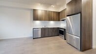Located at 1915 Sooke Rd in Colwood, BC, this thoughtfully designed one-bedroom, one-bathroom unit offers a functional and modern layout across a single floor. The open-concept living, dining, and kitchen area forms the heart of the unit, finished with light wood-look flooring that runs throughout. The kitchen is a standout feature, showcasing rich dark wood cabinetry extending to the ceiling, a white subway tile backsplash, granite countertops with a waterfall edge, track lighting, and a full suite of stainless steel appliances including a dishwasher, electric range, and refrigerator. The bright bedroom is served by a large window with views of the surrounding neighbourhood and benefits from baseboard heating. The clean, white bathroom includes a soaker tub with full-height white tile surround and a wood-toned vanity that complements the kitchen cabinetry. A versatile den provides additional flexible space, ideal for a home office or storage. Three closets, including an in-unit laundry closet, offer generous storage throughout. A private balcony extends the living space outdoors. The unit's crisp white walls, consistent flooring, and modern finishes create a bright, cohesive, and contemporary ambiance.