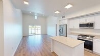 Located at 100 Cortona Point Dr in Goleta, CA, this well-designed 2-bedroom, 2-bathroom single-story home offers a bright and contemporary living experience. The open-concept kitchen and living area serves as the heart of the home, featuring soaring ceilings that amplify the sense of space, light wood-tone flooring, and abundant natural light streaming through large sliding glass doors and clerestory windows. The kitchen is outfitted with crisp white shaker cabinetry, neutral quartz countertops, a stainless steel refrigerator with an ice and water dispenser, a built-in dishwasher, and a center island ideal for meal prep or casual dining. The spacious primary bedroom includes generous walk-in closet space with built-in shelving and rod systems across multiple closets, providing excellent storage. Both bathrooms are finished with wood-look flooring, marble-style tiled tub-shower surrounds with sliding glass or curved rod enclosures, and clean white fixtures. The secondary bedroom is well-proportioned and receives natural light through a window with outdoor views of surrounding greenery. A connecting hallway ties the layout together efficiently. Throughout the home, a neutral color palette and consistent flooring create a cohesive, modern aesthetic.