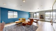 Located at 281 Willow St in Fort Collins, Colorado, this single-floor lounge and game room is a well-appointed communal space designed for both relaxation and recreation. The room is defined by its bold, contemporary aesthetic, highlighted by a striking teal accent wall that anchors the lounge area and a contrasting sage-green wall near the entertainment zone, creating a dynamic and energetic atmosphere throughout.

The space is outfitted with mid-century modern furnishings, including a mustard-yellow sofa, a matching chaise, a sculptural wood coffee table, and a molded wood accent chair, all arranged atop a patterned area rug over light hardwood-style flooring. A wall-mounted flat-screen television with a sleek wood media console serves as the entertainment focal point, accompanied by a large-scale mosaic artwork that adds a vibrant artistic touch to the room.

The game area features a full-size pool table illuminated by a modern linear pendant light, along with a foosball table. A wall-mounted cue rack keeps the space organized and functional. Large floor-to-ceiling windows and glass doors flood the room with abundant natural light and offer expansive views of the surrounding Fort Collins skyline and the Rocky Mountains in the distance, seamlessly connecting the interior to the outdoors.