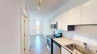 Located at 2015 Lyndale Ave S in the Lyndale neighborhood of Minneapolis, MN, this single-floor unit offers a clean, contemporary design throughout. The galley-style kitchen is well-appointed with stainless steel appliances including an electric range, over-the-range microwave, dishwasher, and refrigerator. White cabinetry with dark accent panels lines the walls, complemented by light stone countertops and a stainless steel sink. Track lighting overhead provides ample illumination, and the layout flows naturally into the open living area. The living space is bright and airy, featuring light wood-style flooring that extends throughout the unit and large windows that invite natural light and frame views of the surrounding Minneapolis cityscape. The bedroom offers a generous, open layout with the same warm flooring and crisp white walls, creating a calm and functional retreat. The bathroom is finished in a bright, minimalist style with white cabinetry, a wide vanity with mirror, and wood-style flooring that ties into the rest of the unit. A stacked washer and dryer unit is conveniently accessible just off the bathroom. The overall aesthetic is modern and clean, with a neutral palette that provides a versatile, move-in-ready living environment.
