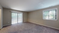 This single-floor residence offers a thoughtfully laid-out living space finished in warm, neutral tones throughout. The living area is generously sized, featuring plush wall-to-wall carpeting and two sources of natural light — a large sliding glass door with vertical blinds that opens to the outdoors, and a side window fitted with blinds. The open feel of the room makes it well-suited for a variety of furniture arrangements. The bedroom is similarly carpeted and bathed in natural light through a window overlooking the exterior greenery, providing a calm and restful atmosphere. The kitchen is a standout feature, showcasing two-tone cabinetry with white upper cabinets and dark lower cabinets, marble-style countertops, a classic white subway tile backsplash, and a stainless steel gas range with a professional-grade range hood. Light wood-look flooring runs through the kitchen, adding warmth to the functional space. The bathroom is clean and well-equipped, featuring a white vanity with a marble-style countertop, a mirror, wood-look tile flooring, a window for natural ventilation, and a full bathtub with a decorative shower curtain. Overall, the space presents a cohesive, move-in-ready environment with practical finishes and comfortable living areas throughout.