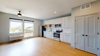 Located at 455 Snelling Ave N in Saint Paul, Minnesota, this thoughtfully designed unit offers a compact yet functional single-floor layout with an open-concept living and kitchen area, one bathroom, and a well-appointed entryway. The interior is finished with light hardwood flooring throughout, contributing to a bright and cohesive aesthetic.

The kitchen runs along one wall and is outfitted with flat-front white cabinetry extending to the ceiling for ample storage, a geometric hexagonal tile backsplash, light wood open shelving, and a full suite of stainless steel appliances including a refrigerator, electric range, built-in microwave, and dishwasher. A black matte faucet and sink anchor the countertop workspace.

The open living area receives natural light through large windows offering outdoor views of the surrounding neighborhood. A ceiling fan is centrally mounted, and wall-mounted HVAC provides climate control.

The entryway features a stylish barn-style door with matte black hardware, a built-in mudroom nook with a slatted wall panel, coat hooks, overhead shelving, and a wood bench — a practical and design-forward touch.

The bathroom is clean and modern, with light wood-tone flooring, a white vanity with dark drawer pulls, a combined tub and shower, and matte black fixture accents throughout. Natural light filters in through a frosted window, completing the fresh, contemporary feel of this well-planned space.