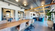 Located at 1720 Nick Nuccio Parkway in Tampa, Florida, this single-floor commercial space blends industrial architecture with contemporary design to create a highly functional and visually dynamic environment. The open floor plan is anchored by polished concrete floors, exposed metal ductwork, and warm wooden ceiling beams that run the length of the space, lending it a refined yet raw aesthetic character.

The main area serves as a versatile gathering and lounge zone, furnished with richly upholstered seating including jewel-toned teal and emerald velvet chairs, a leather sectional sofa, and layered area rugs. Bold large-scale botanical artwork adorns the white walls, adding vibrancy throughout. A long communal wooden conference table with mixed seating provides a dedicated collaboration zone, while a separate bar-height counter with stools and built-in shelving offers additional workspace.

A private office, accessed through a glass-paneled door with black metal framing, features a woven jute rug, a wood desk, warm lamp lighting, and an arched accent niche — providing a quiet, refined retreat within the larger space. The hallway connects the various zones seamlessly.

Black-framed windows throughout flood the interior with natural light and frame views of the surrounding Tampa neighborhood. The overall ambiance is modern, creative, and welcoming — well-suited for professional or community-oriented use.