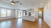 This well-appointed single-floor residence offers a thoughtfully designed open-concept layout with clean, contemporary finishes throughout. The expansive living and kitchen area is anchored by warm wood-look flooring and ceiling fans, creating an inviting and functional shared space. The kitchen stands out with its sleek white quartz countertops, a large center island with an integrated sink, shaker-style cabinetry in a soft gray tone, full-height subway tile backsplash, stainless steel appliances including a French door refrigerator, electric range, and built-in microwave, plus stylish pendant and track lighting overhead. Large windows allow generous natural light to fill the open living area. The bedrooms feature plush carpeting and ceiling fans, with one bedroom offering a walk-in closet and direct access to an en-suite bathroom. The primary bathroom is especially well-equipped, showcasing a dual-sink vanity with granite countertops, gray shaker cabinets, hardwood-style flooring, and a full bathtub and shower combination. A secondary bathroom mirrors the same refined aesthetic with granite countertops, ample cabinetry, and matching fixtures. The overall design emphasizes bright, neutral tones, modern hardware, and practical layouts that maximize comfort and usability throughout the space.