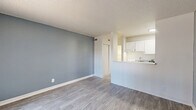 Located at 6300 Montgomery Blvd NE in Albuquerque, NM, this single-floor, one-bedroom, two-bathroom unit offers a practical and well-appointed layout. The living room features light wood-look flooring, a textured ceiling, and a cool blue-gray accent wall that adds a modern touch. A large sliding glass door floods the space with natural light and provides an outdoor view, while a pass-through window connects the living area to the kitchen, which is outfitted with white cabinetry and a full-size refrigerator. The bedroom continues the light flooring theme and showcases a distinctive painted brick accent wall alongside large windows with vertical blinds. A wide three-panel sliding closet provides generous built-in storage, complemented by a track lighting fixture overhead. Two bathrooms serve the unit; one features a full tub-shower combo with clean white subway-style wall tiles and chrome fixtures, while the other includes a vanity with white cabinetry, a countertop sink, and a well-lit mirror. Throughout the unit, consistent light wood-look flooring and neutral tones create a cohesive, clean aesthetic suited for comfortable everyday living.