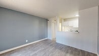 Located at 6300 Montgomery Blvd NE in Albuquerque, NM, this single-floor, one-bedroom, two-bathroom unit offers a practical and well-appointed layout. The living room features light wood-look flooring, a textured ceiling, and a cool blue-gray accent wall that adds a modern touch. A large sliding glass door floods the space with natural light and provides an outdoor view, while a pass-through window connects the living area to the kitchen, which is outfitted with white cabinetry and a full-size refrigerator. The bedroom continues the light flooring theme and showcases a distinctive painted brick accent wall alongside large windows with vertical blinds. A wide three-panel sliding closet provides generous built-in storage, complemented by a track lighting fixture overhead. Two bathrooms serve the unit; one features a full tub-shower combo with clean white subway-style wall tiles and chrome fixtures, while the other includes a vanity with white cabinetry, a countertop sink, and a well-lit mirror. Throughout the unit, consistent light wood-look flooring and neutral tones create a cohesive, clean aesthetic suited for comfortable everyday living.