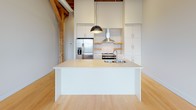 Located at 326 W Florida St in Milwaukee's vibrant Walker's Point neighborhood, this single-floor loft masterfully blends historic industrial character with contemporary design. The open-concept layout is anchored by striking exposed wood beam ceilings and original timber post-and-beam framing, which contrast beautifully against crisp white walls and smooth light hardwood flooring that runs throughout the space.

The kitchen serves as a focal point, featuring a large waterfall-edge island with an integrated sink, sleek white cabinetry extending to ceiling height, stainless steel appliances including a French door refrigerator and range, a wall-mounted range hood, and a classic subway tile backsplash with open wood shelving accents. A bold pendant light anchors the island, adding a modern industrial touch.

The main living area is generously proportioned, offering an expansive, flexible layout bathed in natural light from tall arched windows framed by exposed brick — a nod to the building's historic roots. Views of the surrounding Milwaukee neighborhood are visible through these architecturally distinctive windows.

The bathroom is clean and functional, finished with light gray tile flooring, accessible grab bars, a soaking tub, and a glass-enclosed shower, maintaining the space's refined, modern aesthetic. The overall ambiance is bright, airy, and full of character.