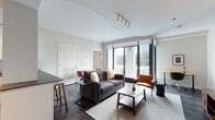 The Peach is a thoughtfully designed two-bedroom, two-bathroom residence located in Atlanta's vibrant Midtown neighborhood. The single-floor layout flows seamlessly from the kitchen through the living area, creating an open and functional living environment throughout.

The living room serves as the heart of the space, featuring dark hardwood flooring, track lighting, and floor-to-ceiling glass doors that lead to a private balcony overlooking the Atlanta cityscape. Natural light fills the room, complementing the contemporary furnishings and neutral color palette. A dedicated workspace area with a desk is also incorporated into the living space.

The kitchen is outfitted with white cabinetry, dark countertops, a subway tile backsplash, and stainless steel appliances, including a range, microwave, and sink — offering a clean, modern aesthetic suited for everyday cooking.

Both bedrooms are comfortably sized and feature dark hardwood floors, upholstered panel headboards, and large windows allowing ample natural light and city views.

The two bathrooms are finished with marble-style tile. One features a glass-enclosed walk-in shower, while the other includes a soaking tub with tiled surround and a white vanity with dark countertop.