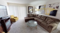 This single-floor residence offers a thoughtfully arranged layout with distinct living, sleeping, cooking, and bathing areas. The living room is generously sized, featuring soft wall-to-wall carpeting, a large L-shaped sectional sofa, and an octagonal glass-top coffee table with a brass frame. Vertical blinds covering a wide sliding door allow for controlled natural light, while bold abstract wall art adds a contemporary visual element to the space.

The kitchen is notably updated, showcasing dark granite countertops, gray cabinetry, a subway tile backsplash, and hardwood-style flooring. Stainless steel appliances — including a French door refrigerator, gas range, built-in microwave, and dishwasher — complete the modern aesthetic.

The bedroom accommodates a queen-size bed and includes a mirrored closet with a built-in rod for organized storage. Neutral carpet, framed wall art, and ample dresser space contribute to a calm, functional environment. A hallway connects the bedroom to the rest of the unit.

The bathroom features a granite-topped vanity with white cabinetry, a large mirror, tile flooring, and a shower-tub combination, maintaining a clean and practical design throughout.