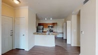 This single-story unit offers a thoughtfully designed layout that maximizes functionality within a compact footprint. The open-concept living and kitchen area creates a seamless flow upon entry, anchored by a curved peninsula with granite-style countertops that doubles as a breakfast bar. The kitchen is well-equipped with rich warm-toned wood cabinetry, stainless steel appliances including a refrigerator, electric range, and over-the-range microwave, complemented by a tile backsplash and ample counter space. Track lighting illuminates the kitchen area, while crown molding adds a refined architectural detail throughout.

Wood-style plank flooring runs consistently throughout the unit, providing a cohesive and easy-to-maintain surface. The bedroom is a generously proportioned space featuring a ceiling fan, a window with plantation-style blinds that allows for natural light and outdoor views, and a six-panel closet door. Neutral wall tones throughout the unit contribute to a bright and clean ambiance.

The bathroom includes a full soaking tub with a tiled shower surround, complemented by wood-style flooring and a vanity with dark wood cabinetry, offering practical storage and a polished finish.