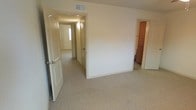 This two-floor property offers a straightforward and functional layout designed for comfortable everyday living. The interiors are finished with wall-to-wall carpeting in a neutral beige tone, contributing to a warm and understated aesthetic throughout the space. Walls are painted in soft, light shades that help maximize the sense of openness and brightness in each room.

The layout features well-connected rooms accessible via a central hallway, allowing for easy movement between areas. Doorways are framed with clean, white paneled doors that complement the overall neutral color palette. A ceiling-mounted HVAC vent is visible, indicating a centralized climate control system for year-round comfort. Wall-mounted light fixtures provide practical illumination in the hallway areas.

Additional rooms visible from the main space include what appears to be a closeted area or storage space, adding to the property's organizational utility. The multi-door configuration suggests a thoughtful separation of living areas across the floor plan, offering both privacy and connectivity.

Spanning two floors, the property provides ample space for varied uses, with the upper and lower levels likely serving distinct functional purposes. The clean, move-in-ready condition of the interiors reflects a well-maintained space ready for occupancy.