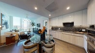 This contemporary high-rise residence offers a thoughtfully designed, single-level layout that seamlessly integrates style and function. Wide-plank hardwood flooring flows throughout the open-plan living, dining, and kitchen areas, creating a warm and cohesive aesthetic. The entryway welcomes visitors with a sleek console and a large round mirror, leading into a generous living space anchored by a plush sofa, accent chairs, and bold artwork that adds a curated, artistic touch.

The kitchen is a standout, featuring light wood and high-gloss white cabinetry, dark granite countertops and backsplash, stainless steel appliances including double wall ovens, and a gas cooktop. A round glass dining table sits adjacent, illuminated by a modern chandelier, with expansive city views framed by floor-to-ceiling windows nearby.

The primary bedroom is a serene retreat highlighted by a textured feature wall, a statement gold pendant light, and a large corner window offering sweeping panoramic views of the city skyline and beyond. The en-suite bathroom features marble-clad walls and floors, a deep soaking tub, and a floating wood vanity. A second bathroom doubles as a laundry room, equipped with a stacked washer and dryer, mosaic tile accents, and clean white finishes throughout.
