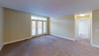 Located at 1302 Eisenhower Rd in Valparaiso, Indiana, this single-floor unit offers a thoughtfully designed layout that balances comfort and functionality. The open-concept living and dining area is generously sized, featuring warm neutral-toned walls, plush carpeting, and a chandelier overhead that adds a touch of elegance. A set of French doors with transom windows floods the living space with natural light and provides access to an outdoor area. The kitchen is well-appointed with rich cherry wood cabinetry, a double-basin sink, laminate countertops, and white appliances including a refrigerator, range, and microwave. Wood-look flooring runs throughout the kitchen, which also connects conveniently to a laundry area. The bedroom is spacious and carpeted, featuring a bright window and direct access to a walk-in closet with built-in shelving. The bathrooms are finished with warm beige tile flooring and include a full tub-shower combination with a curved curtain rod, a toilet, and a wood-toned vanity. The consistent warm color palette and clean finishes throughout the unit create a welcoming and cohesive living environment.