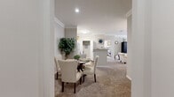 This single-floor residence offers a thoughtfully designed layout that balances comfort and functionality. The open-plan living and dining area serves as the heart of the home, where soft carpeting, crown molding, and neutral warm-gray walls create an inviting atmosphere. The living room benefits from large windows dressed with white blinds that allow generous natural light to fill the space, complemented by a ceiling fan overhead. Adjacent to the living area, the dining space comfortably accommodates a round table with upholstered chairs, making it ideal for everyday meals or entertaining.

The galley-style kitchen features white cabinetry, white appliances including a full-size refrigerator and range, a double sink, and rich wood-look flooring that contrasts cleanly with the bright cabinetry. A dedicated entry door provides direct access from the kitchen area.

The two bedrooms are carpeted and generously proportioned, each offering ample space for full furniture arrangements. One bedroom includes a built-in desk area, adding versatile utility to the room.

Two full bathrooms serve the residence, both featuring tub-shower combinations, wood-look flooring, and white vanities with light countertops. One bathroom includes a window for added natural light and ventilation. Throughout the home, the consistent use of neutral tones, crown molding, and quality finishes contributes to a cohesive and polished aesthetic.