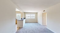 This single-floor residence offers a practical and well-organized layout across two bedrooms and two bathrooms. The open-concept living and dining area is finished with neutral-toned carpet and warm beige walls, creating a bright and cohesive atmosphere. Multiple windows along the exterior wall allow generous natural light to fill the space throughout the day.

The kitchen is positioned adjacent to the living area and defined by a peninsula with dark countertops that serves as both a workspace and a visual divider. Warm wood-toned cabinetry lines the walls, complemented by white appliances including a range and refrigerator. Tile flooring in the kitchen provides a clean contrast to the carpeted living areas.

The spacious primary bedroom features two side-by-side closets offering ample storage, along with a window framing outdoor views. The second bedroom is similarly well-lit, with multiple windows and plush carpet underfoot. Both bathrooms are functional in design; one features a tiled tub-shower combination with tile flooring, while the other includes a single vanity with wood cabinetry and a bright window. A connecting hallway ties all rooms together efficiently.