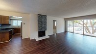 Located at 200 City Blvd W in Orange, California, this single-floor residence offers a well-designed layout with a cohesive blend of functional spaces and comfortable finishes throughout. The expansive living area is anchored by a striking floor-to-ceiling tiled fireplace and flows seamlessly toward sliding glass doors that open to a private balcony, allowing natural light to fill the room. Rich, dark hardwood-style flooring extends across the main living and dining areas, adding warmth and visual continuity. The kitchen features warm wood cabinetry, dark granite-style countertops, a patterned tile backsplash, stainless steel appliances, and a peninsula that opens to the dining area, which is accented by a pendant light fixture. Bedrooms are finished with plush carpeting and neutral taupe walls beneath textured ceilings, offering a quiet retreat. One bedroom benefits from plantation shutter windows that provide both natural light and privacy. The bathroom includes a white vanity with dark granite countertop, a large mirror with overhead lighting, and a glass-enclosed shower and tub combination. A second bathroom offers a sleek sliding glass shower enclosure. Throughout the residence, textured ceilings and neutral tones create a consistent, understated aesthetic suited to a variety of living arrangements.