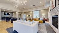 Located at 3400 Club Way Ct in Powell, Ohio, this generously sized single-floor amenity space offers a sophisticated and welcoming environment designed for social gatherings and community events. Wide-plank hardwood flooring flows throughout the main open area, anchoring the space with warmth and continuity.

The lounge area is a standout feature, highlighted by soaring ceilings adorned with striking starburst chandeliers and a floor-to-ceiling stacked stone fireplace that serves as a dramatic focal point. Plush seating arrangements in bold mustard, white, and rust tones create an inviting atmosphere, while large windows flood the space with natural light and offer views of the surrounding neighborhood.

The dining zone accommodates multiple seating configurations, featuring a mix of sleek dining tables with upholstered chairs arranged around a central open floor plan. Adjacent to the dining area is a well-appointed wet bar with a white quartz countertop, patterned cabinetry, a tiled backsplash, and a row of bar stools beneath conical pendant lights.

A separate tiled utility or service room with built-in cabinetry provides additional functional space. Neutral gray walls, crown molding, and recessed lighting unify the design throughout, creating a polished, modern aesthetic that balances comfort with elegance.