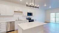 Located at 6155 24th St S in Fargo, North Dakota, this well-designed one-bedroom, two-bathroom unit offers a thoughtfully arranged single-floor layout that maximizes every square foot. The open-concept kitchen and living area serves as the heart of the home, featuring crisp white shaker cabinetry extending to the ceiling, stainless steel appliances including a French door refrigerator, electric range, built-in microwave, and dishwasher. A white quartz center island provides additional prep and seating space, while a multi-pendant chandelier and recessed lighting lend a polished, modern touch. Light-toned luxury vinyl plank flooring runs throughout the main living areas, complementing the bright, neutral palette. The living room is anchored by a sliding glass door that fills the space with natural light and provides outdoor access. The bedroom is carpeted for comfort, features a generous window with outdoor views, and connects directly to a dedicated closet and an en-suite bathroom. The en-suite bath is finished with a white shaker vanity, quartz countertop, undermount sink, and matte black fixtures, echoing the home's consistent modern aesthetic. A second full bathroom serves guests. A hallway with additional storage ties all spaces together, creating a clean and functional flow throughout this contemporary Fargo residence.