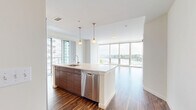 Located at Harbor Point in Stamford, CT, this well-appointed 2-bedroom, 2-bathroom residence offers a thoughtfully designed open-concept layout with rich hardwood flooring throughout. The combined kitchen and living area serves as the heart of the home, anchored by a large center island with a white quartz countertop, an undermount sink, and elegant pendant lighting overhead. The kitchen is outfitted with full-height wood cabinetry and a complete suite of stainless steel appliances, including a gas range, built-in microwave, refrigerator, and dishwasher. Floor-to-ceiling windows bathe the living area in natural light and frame sweeping views of the harbor and marina below, with a private balcony extending the living space outdoors. Both bedrooms continue the hardwood flooring and are served by large windows — the primary bedroom offering generous proportions and ample closet space. The two bathrooms feature wood-toned vanities with white countertops, tiled flooring, and clean, modern fixtures. Three closets throughout the residence provide excellent storage. A connecting hallway ties the layout together efficiently. The overall ambiance is bright, modern, and sophisticated, with waterfront views as a defining highlight.