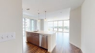Located at Harbor Point in Stamford, CT, this well-appointed 2-bedroom, 2-bathroom residence offers a thoughtfully designed open-concept layout with rich hardwood flooring throughout. The combined kitchen and living area serves as the heart of the home, anchored by a large center island with a white quartz countertop, an undermount sink, and elegant pendant lighting overhead. The kitchen is outfitted with full-height wood cabinetry and a complete suite of stainless steel appliances, including a gas range, built-in microwave, refrigerator, and dishwasher. Floor-to-ceiling windows bathe the living area in natural light and frame sweeping views of the harbor and marina below, with a private balcony extending the living space outdoors. Both bedrooms continue the hardwood flooring and are served by large windows — the primary bedroom offering generous proportions and ample closet space. The two bathrooms feature wood-toned vanities with white countertops, tiled flooring, and clean, modern fixtures. Three closets throughout the residence provide excellent storage. A connecting hallway ties the layout together efficiently. The overall ambiance is bright, modern, and sophisticated, with waterfront views as a defining highlight.