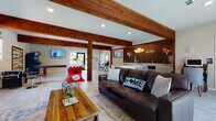 This single-story community clubhouse blends rustic charm with modern design, creating an inviting and versatile gathering space. Prominent exposed wooden beams run throughout the open-plan interior, anchoring the space with warmth and architectural character. Light wood-look tile flooring extends across the entire layout, enhancing the bright, airy atmosphere.

The main lounge area features rich leather sofas, layered area rugs, and Texas-inspired accent pillows, centered around a striking stone fireplace with a chunky wood mantle and a wall-mounted flat-screen TV. Large windows and glass doors allow generous natural light and outdoor views into this relaxed seating zone.

Adjacent to the lounge is a well-appointed bar area, defined by a bold dark subway tile accent wall, antler-style chandeliers, a spacious granite-topped island with bar seating, and ample white cabinetry with countertop workspace. Multiple flat-screen TVs make this an ideal spot for social gatherings.

The dedicated game room offers an expansive open floor plan accommodating a foosball table, shuffleboard table, and an arcade machine, with additional windows providing natural light and outdoor views. A restroom with light tile flooring, neutral tones, and accessibility features rounds out the space, ensuring comfort and convenience for all visitors.