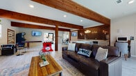 This single-story community clubhouse blends rustic charm with modern design, creating an inviting and versatile gathering space. Prominent exposed wooden beams run throughout the open-plan interior, anchoring the space with warmth and architectural character. Light wood-look tile flooring extends across the entire layout, enhancing the bright, airy atmosphere.

The main lounge area features rich leather sofas, layered area rugs, and Texas-inspired accent pillows, centered around a striking stone fireplace with a chunky wood mantle and a wall-mounted flat-screen TV. Large windows and glass doors allow generous natural light and outdoor views into this relaxed seating zone.

Adjacent to the lounge is a well-appointed bar area, defined by a bold dark subway tile accent wall, antler-style chandeliers, a spacious granite-topped island with bar seating, and ample white cabinetry with countertop workspace. Multiple flat-screen TVs make this an ideal spot for social gatherings.

The dedicated game room offers an expansive open floor plan accommodating a foosball table, shuffleboard table, and an arcade machine, with additional windows providing natural light and outdoor views. A restroom with light tile flooring, neutral tones, and accessibility features rounds out the space, ensuring comfort and convenience for all visitors.