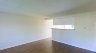 This single-floor space presents a straightforward and functional interior design. The main living area is characterized by rich, dark hardwood-style flooring that grounds the room and adds warmth to the overall aesthetic. The floors contrast cleanly with the neutral, light-toned walls, which are finished in a soft off-white palette that creates a bright and open atmosphere.

The ceiling features a classic popcorn texture, a common architectural detail that adds subtle visual interest overhead. White baseboards run along the perimeter of the room, providing a crisp, clean border between the walls and flooring and contributing to the space's tidy appearance.

Electrical outlets are positioned at standard intervals along the walls, offering practical utility throughout the room. The space is notably open and unfurnished, allowing for a wide range of layout and design possibilities. The minimalist, move-in-ready condition of the interior makes it highly adaptable to various uses and personal styles. Overall, the space conveys a clean, neutral ambiance suited for comfortable everyday living.